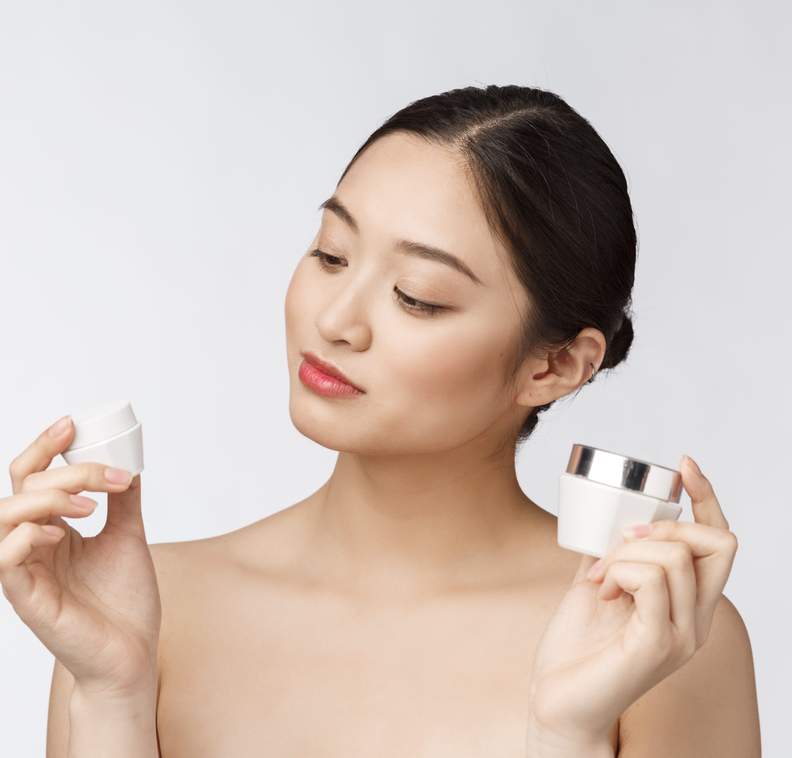 Beautiful young woman on white isolated background holding cosmetic face cream, asian.